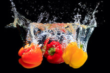 Red, Orange And Yellow Peppers Splashing Water On Black Background