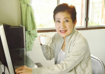 Asian elder woman enjoy her coffee while working with personal computer