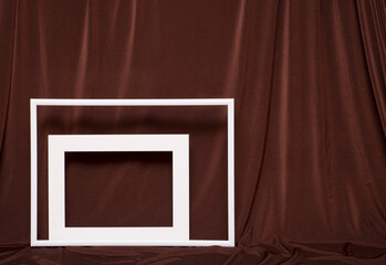 Two empty picture frames on background of brown cloth.