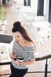 © romankosolapov - Attractive young woman writing in her notebook while standing on stairs in a cafe and looking down.