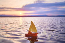 A Small Children's Yellow Red Boat Sails On The Sea Against The Background Of The Sunrise
