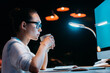 © LIGHTFIELD STUDIOS - Side view of young businesswoman in eyeglasses holding cup while working late in office