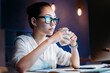 © LIGHTFIELD STUDIOS - Young businesswoman in eyeglasses holding cup while working late in office