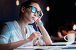 © LIGHTFIELD STUDIOS - Young businesswoman in eyeglasses holding pencil and working late in office