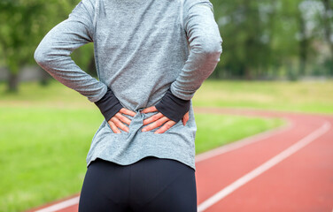 Wall Mural - Athletic woman on running track touching hurt back with painful injury