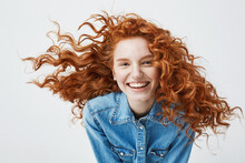 Portrait Of Beautiful Cheerful Redhead Girl With Flying Curly Hair Smiling Laughing Looking At Camera Over White Background.