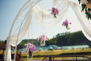 Poster - Glass bottles with pink flowers hang from wedding altar
