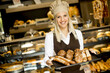 Beautiful female bakery posing with various types of pastries and breads in the baker shop