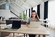© romankosolapov - Photo of young cheerful lady sitting in office coworking while using laptop computer chatting by phone. Looking at camera.