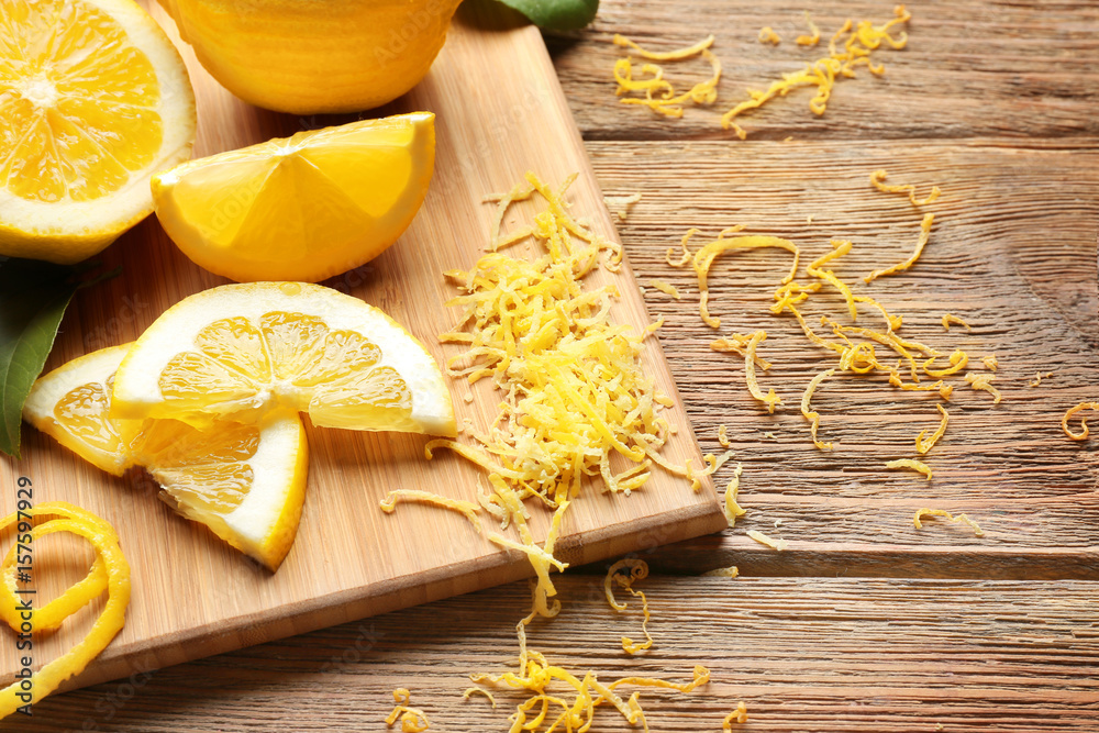 Board with cut lemons and zest on wooden table, closeup