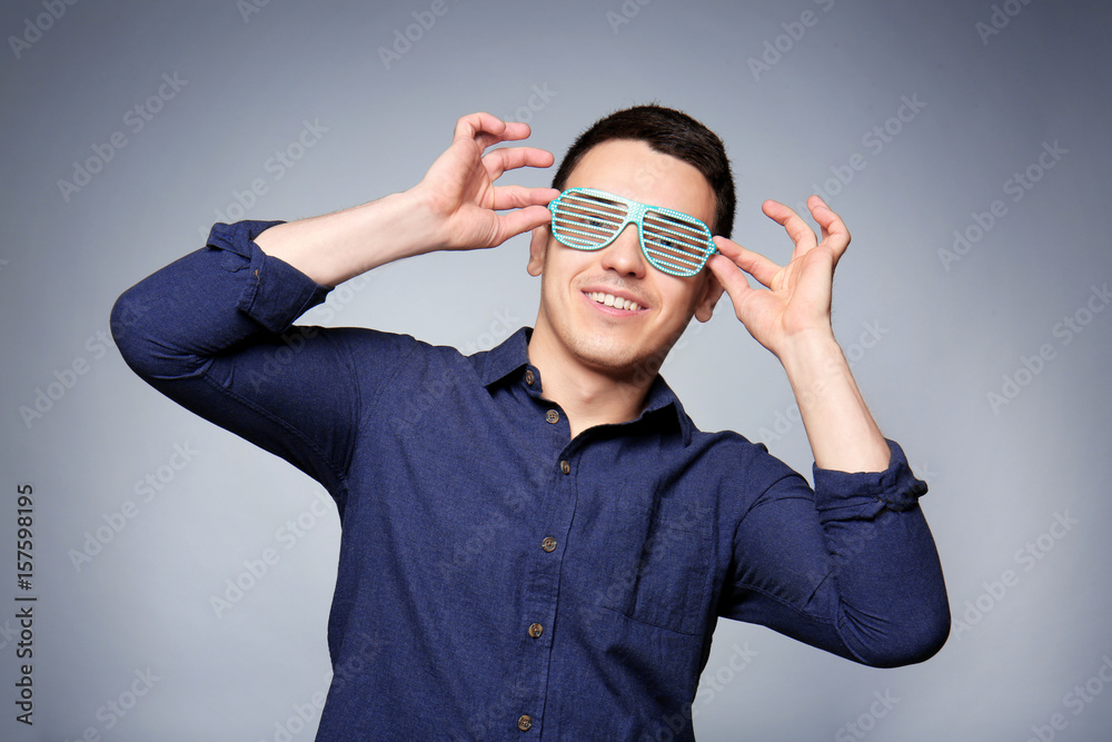 Happy young man with party glasses on gray background