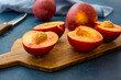 Ripe juicy nectarines, whole and halved on wood cutting board, knife, blue kitchen towel, modern minimalist style
