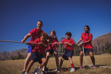 Wall Mural - trainer assisting kids in tug of war during course