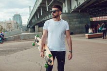 Stylish Man In Sunglasses And With A Beard Stands On The Street With A Long Board. T-shirt Mock Up.