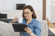 Mature woman using tablet computer while relaxing on sofa at home
