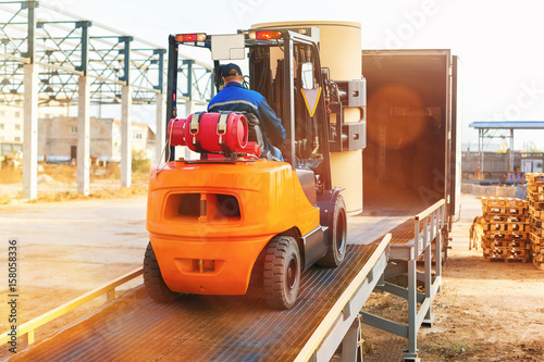 Fototapeta Forklift is putting cargo from warehouse to truck outdoors