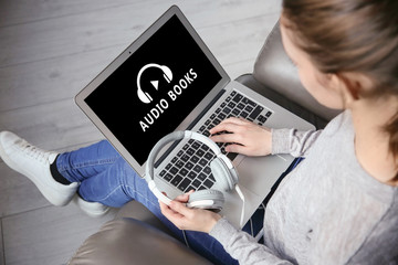 Wall Mural - Concept of audio books and modern technology. Woman sitting in armchair and using laptop with headphones