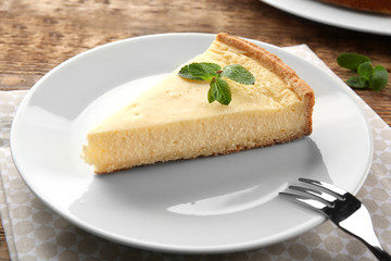 Poster - Plate with piece of tasty cheesecake on wooden table, closeup