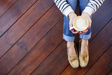 Woman Holding In Hands Cup Of Coffee With Milk Sitting On The Floor