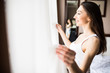 © F8  \ Suport Ukraine - Young woman opens curtains to look at the view from a window in the morning
