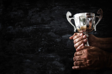 Wall Mural - low key image of a man holding a trophy cup over dark background