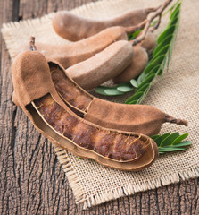 Canvas Print - Sweet ripe tamarind pods with tamarind leaves on wood background