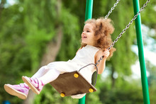 Child Swinging On A Swing At  Playground In The Park. Children Protection Day.