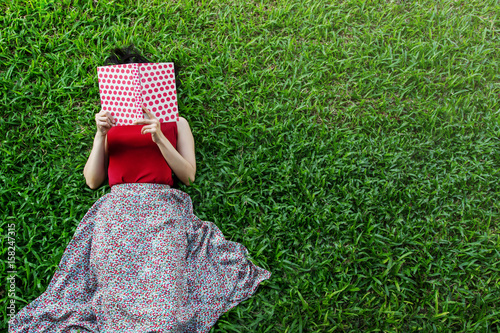 Fotografía Woman lay down or relaxing on green grass reading book in summer or spring, top