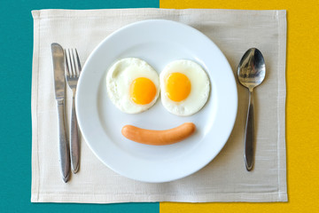 Smiling face frying eggs breakfast on a white plate isolated on green and yellow background.