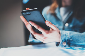 Closeup view of female hands holding modern mobile phone and pointing fingers on the touch screen.Horizontal, blurred background, bokeh effects.