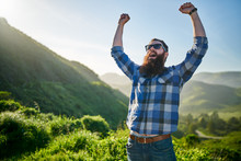 Excited Man With Beard And Sunglasses Cheering In Front Of Grassy Green Hills In California
