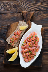 Wall Mural - Above view of a glass plate with salmon tartare on a rustic wooden background, studio shot