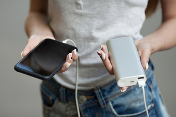 girls hands hold of the phone and charger. Powerbank and smartphone in girl's hands. Energy charger power bank smart phone. Still life modern digital concept.