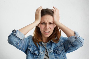 Wall Mural - Unhappy frustrated student girl clenching teeth, having painful look, grimacing, squeezing temples, suffering from migraine or headache, feeling stressed while facing problems at university.