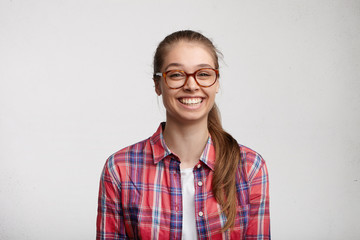 People and lifestyle. Youth and happiness. Carefree happy teenage girl in stylish wear and eyeglasses can't help but laugh while watching good comedy on TV, standing against blank wall background