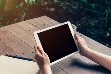 Woman hand holding tablet and blank screen display on wood table in coffee shop.