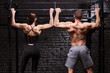 Rear view photo of couple of man and woman in the sportwear making exercise on a horizontal bar against brick wall.