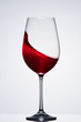 © Aleksey - Splashing red wine with wave in the elegant wineglass standing against light background with reflection.