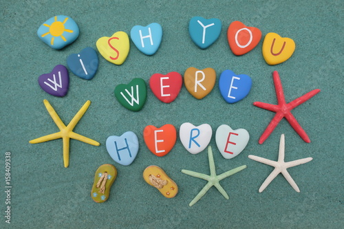 Fotografía Wish you were here with colored stone hearts over green sand