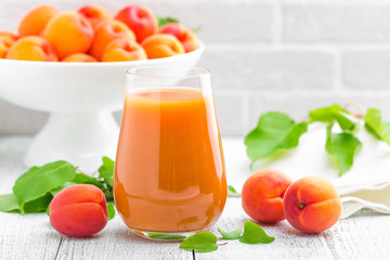 Wall Mural - Apricot juice and fresh fruits with leaves on white wooden table