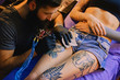 © Fxquadro - Bearded tattoo male artist makes a tattoo on a female leg.
