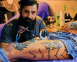 © Fxquadro - The bearded tattoo artist makes a tattoo on a woman's leg in an ink saloon.