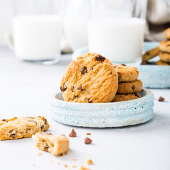 Wall Mural - Stack of chocolate chip cookies on blue stone plate with glass of milk on light gray background. Selective focus. Copy space.