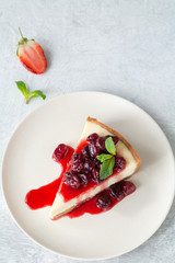 Wall Mural - Slice of plain cheesecake with berry sauce decorated with mint leaf on a plate over bright concrete background and copy space. Top view