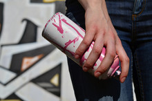 Photo Of A Girl's Hand With Aerosol Paint Cans In Hands On A Graffiti Wall Background. The Concept Of Street Art And Use Of Aerosol Paints. Graffiti Art Shop Background Image
