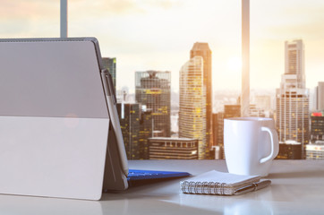 Convertible laptop on table in office with panoramic sunset view of modern downtown skyscrapers at business district