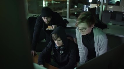 Wall Mural - young hacker typing something on computer in the dark office. his colleagues standing behind him and