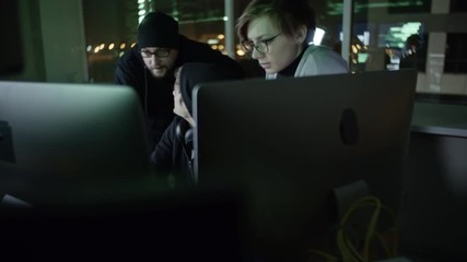 Wall Mural - tilt up of young hacker typing something on computer and discussing something with male and female p