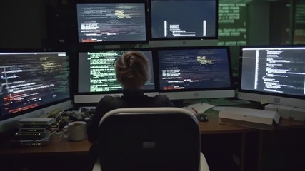 Wall Mural - rear view of female hacker sitting in the dark office in front of six monitors with data