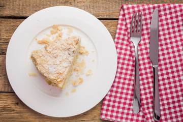 Wall Mural - cake Napoleon on a white plate, on a wooden background and a red-white napkin